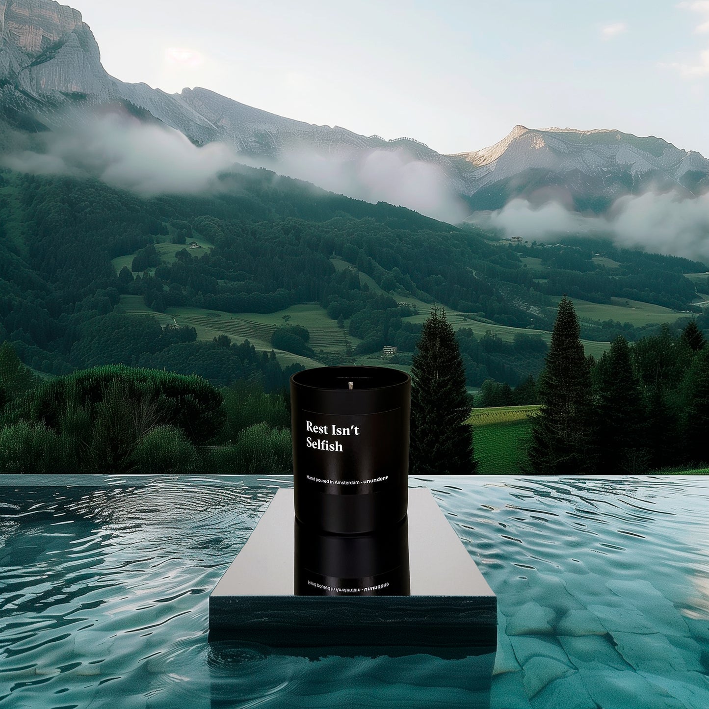 Unundone’s aromatherapy candle “Rest Isn’t Selfish” standing in a pool, with Italian hills and mountains in the distance