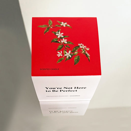 Top view of Unundone’s candle box with botanical illustration and affirmation "You're Not Here to Be Perfect."