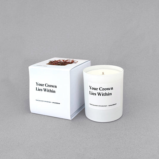 Unundone’s ‘Your Crown Lies Within’ candle with its box, featuring a crown and flower design, photographed on a grey studio background.