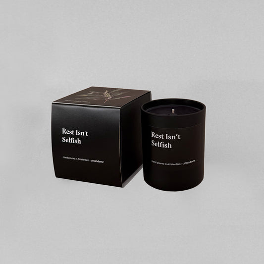 Black aromatherapy candle “Rest Isn’t Selfish” in glass jar with matching black box, styled on a grey studio background.