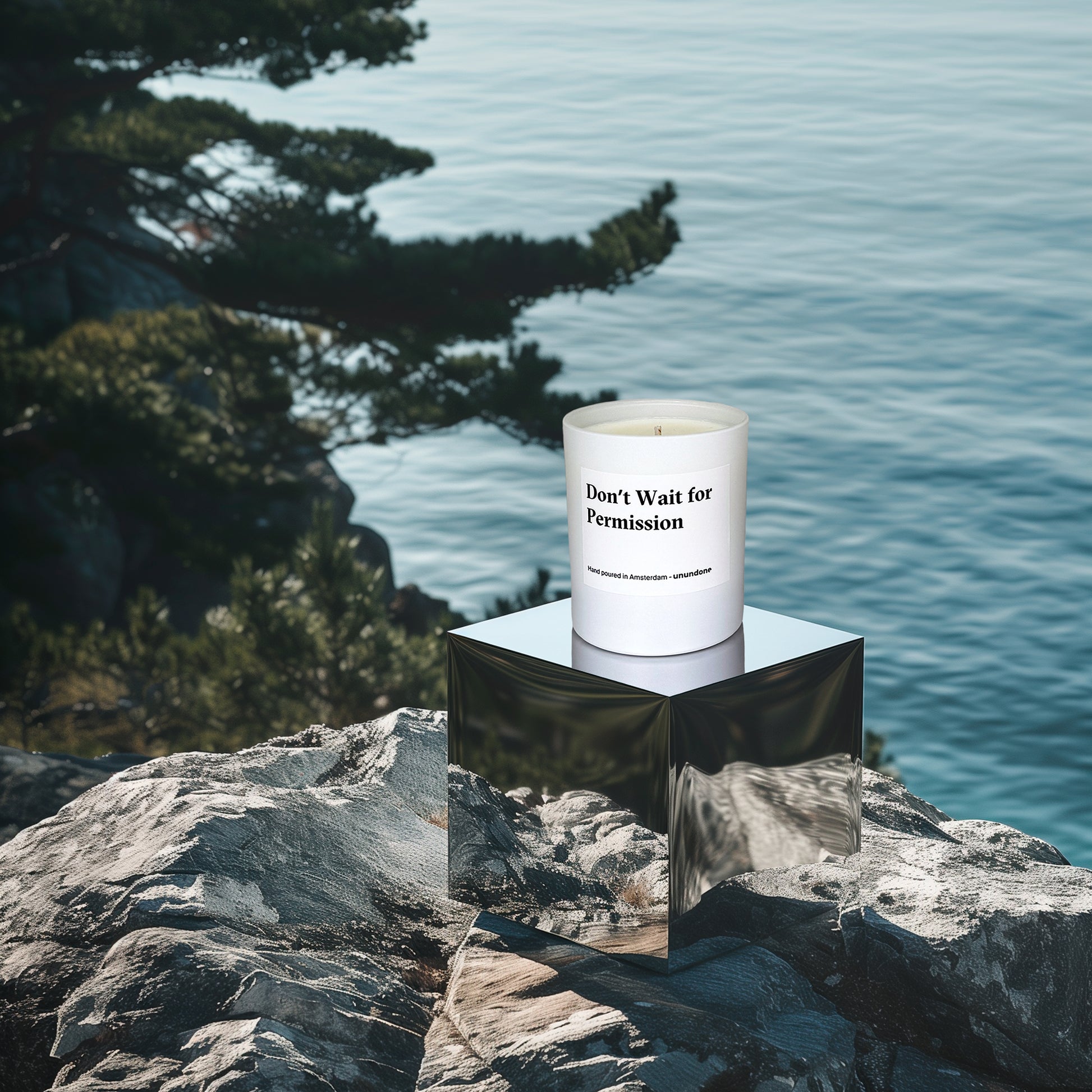 Unundone candle “Don’t Wait for Permission” on reflective cube podium beside pine tree and seashore backdrop.