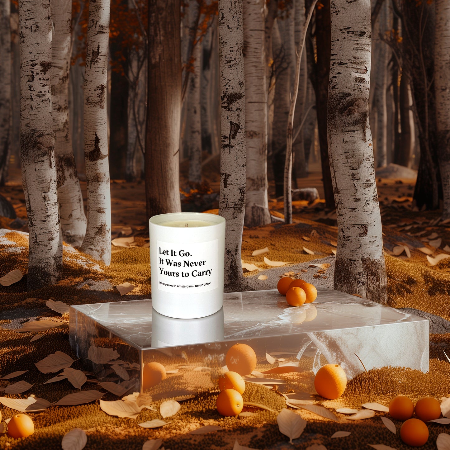 Candle “Let It Go, It Was Never Yours to Carry” placed on reflective podium among fallen leaves, oranges, and birch trees.